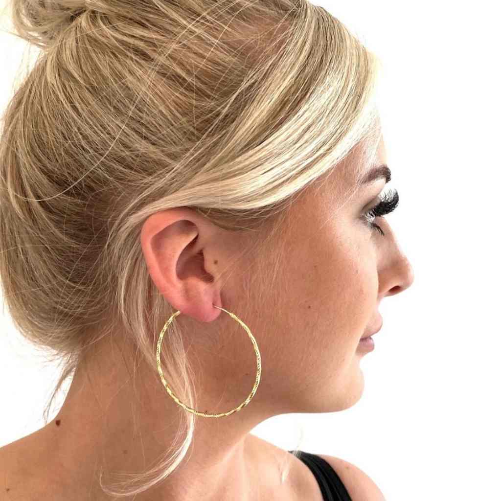 Attractive blonde lady wearing a large pair of gold hoop earrings. The hoops are sparkling in the light.