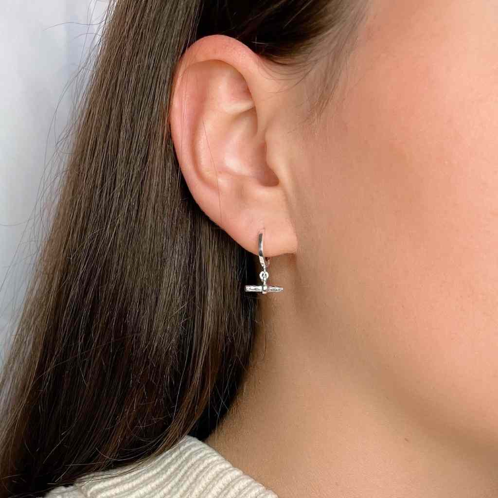 Model wearing sterling silver huggie earrings. Features a T-bar drop with a high shine,